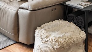 Ein beiges Ledersofa mit passendem Hocker und einem kleinen Beistelltisch, auf dem sich eine Pflanze und eine Zeitschrift befinden.