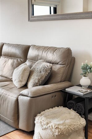A beige leather sofa with a matching ottoman and a small side table with a plant and a magazine. - Colley Escape Vibrant Life on Glenelgs Foreshore (Glenelg)