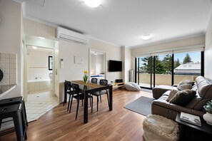 A modern living room with a dining area, a sofa, a TV, and a balcony with a view. - Colley Escape Vibrant Life on Glenelgs Foreshore (Glenelg)
