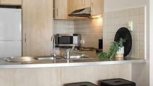 Eine moderne Küche mit Holzschränken, einer Edelstahlspüle, einer Mikrowelle und einer Uhr an der Wand.