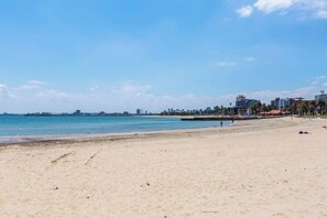 Ein sandiger Strand mit blauem Himmel und einer entfernten Skyline.