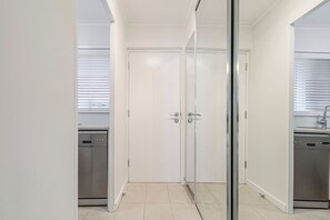 Eine Küche mit Geschirrspüler, einer weißen Tür mit Griff und einem Fenster mit Jalousien.