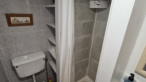 Kylpyhuone, jossa on wc, suihku ja hylly, jossa on hygieniatuotteita.