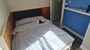 Makuuhuone, jossa on sänky, ovi ja sininen seinä, jossa on hylly.