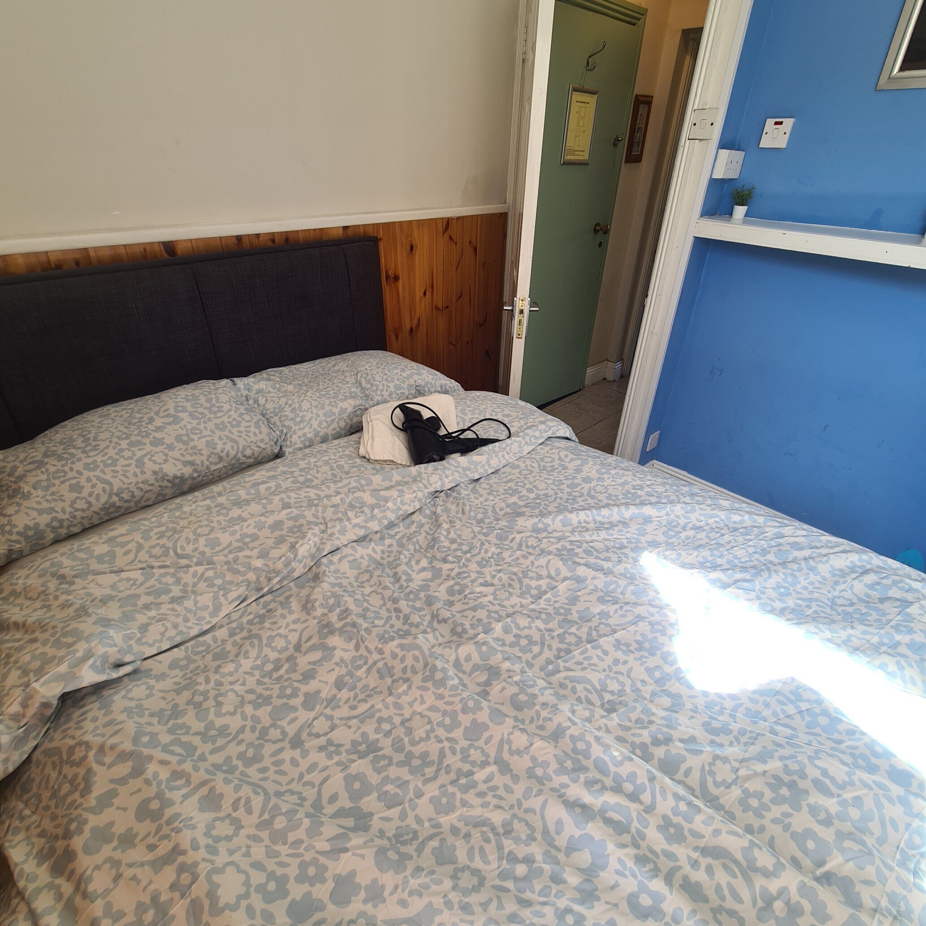 A bed with a patterned bedspread, a bedside table with a lamp, and a door with a light switch.