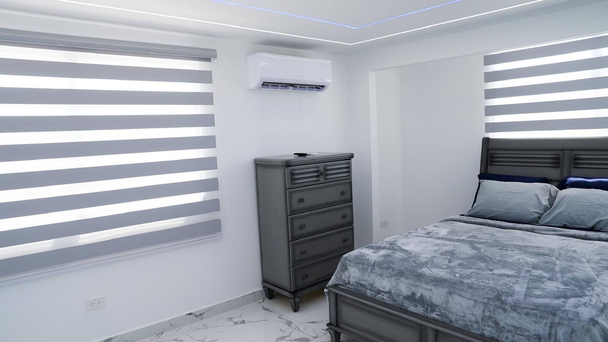A bedroom with a bed, dresser, and air conditioning unit.