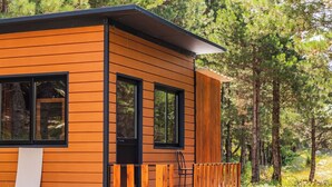 Une cabane moderne en bois, dotée de grandes fenêtres, d’une terrasse et donnant sur une forêt.