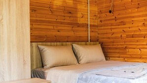 A wooden-paneled room with a bed, a nightstand, and a wall-mounted light fixture.