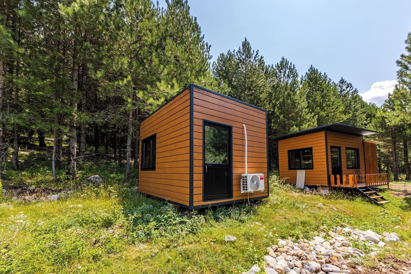 Two wooden cabins in a forested area with a clear sky.
