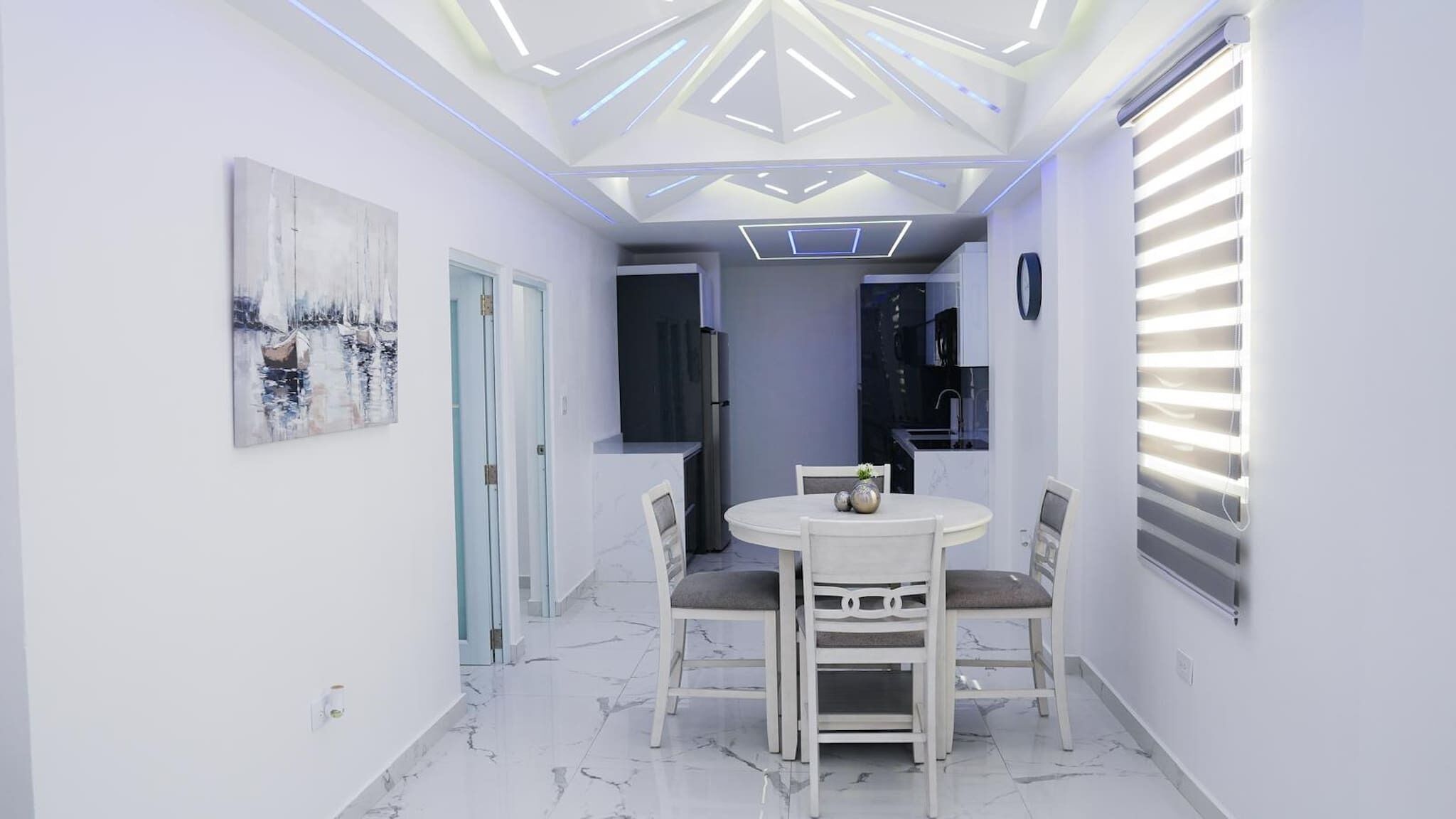 Eine moderne Küche mit integriertem Backofen, ein Essbereich mit rundem Tisch und Stühlen sowie eine Decke mit geometrischen Leuchten.