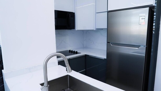 A modern kitchen with a stainless steel refrigerator, a black microwave, and a white countertop. - Stunning & Cozy 2-Bedroom San Juan Apartment (San Juan)