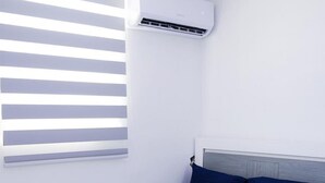 A bedroom with a bed, a window with blinds, an air conditioning unit, and a light fixture. - Stunning & Cozy 2-Bedroom San Juan Apartment (San Juan)