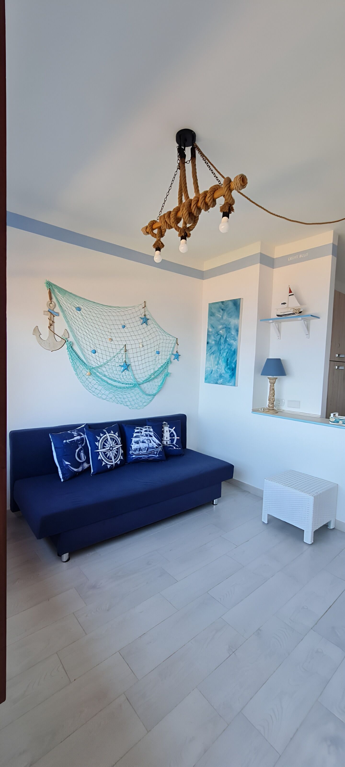 A modern living room with a blue sofa, nautical-themed wall art, and a chandelier.
