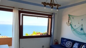Una stanza con una grande finestra, un divano blu, un tavolo bianco e un lampadario.