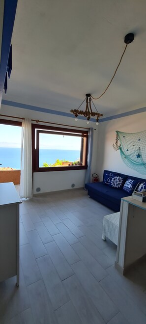 Ein Zimmer mit großem Fenster, einem blauen Sofa, einem weißen Tisch und einer Deckenleuchte.