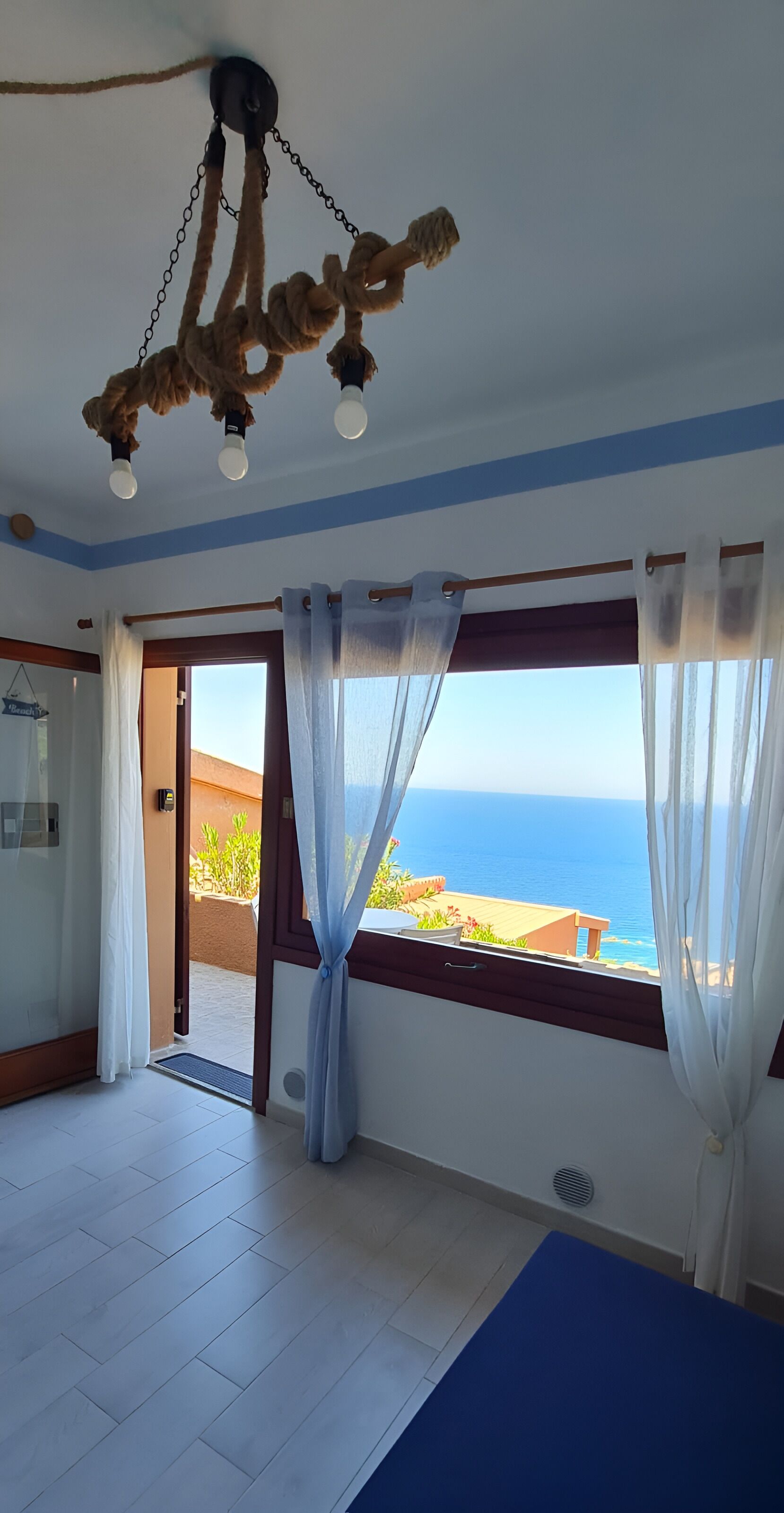 Una habitación con vista al mar, un lámpara en el techo y una puerta que da al exterior.