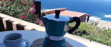 Una mesa con una cafetera y una taza, con vistas a la costa.