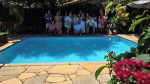 Ein Schwimmbecken mit Steinbord, umgeben von Grünpflanzen und einem Gebäude im Hintergrund.