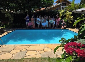 A swimming pool with a stone border, surrounded by greenery and a building in the background. - A cozy retreat in Búzios. Just a few minutes' walk from the resort's best beach. (Armação dos Búzios)
