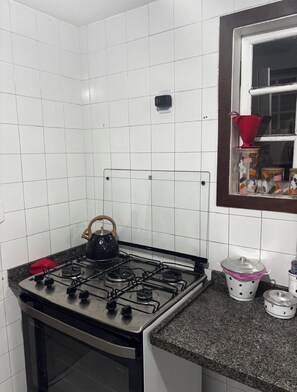A kitchen with white tiled walls, a gas stove, a kettle, and a window with a view of the outside. - A cozy retreat in Búzios. Just a few minutes' walk from the resort's best beach. (Armação dos Búzios)