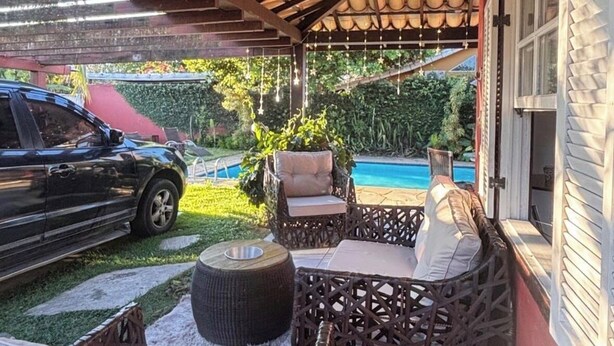 Eine Terrasse im Freien mit Korbmöbeln, einem Pool und einem in der Nähe stehenden Auto.