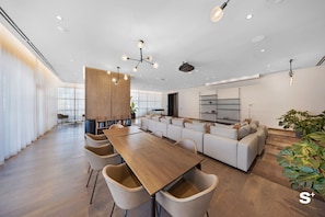 A modern interior with a wooden dining table, beige chairs, a sofa, and a large window. - Downtown Studio Near Kaseya - Pool & Gym (Miami)