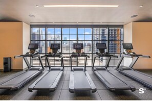 A gym with treadmills, exercise screens, and a city view through large windows. - Downtown Studio Near Kaseya - Pool & Gym (Miami)
