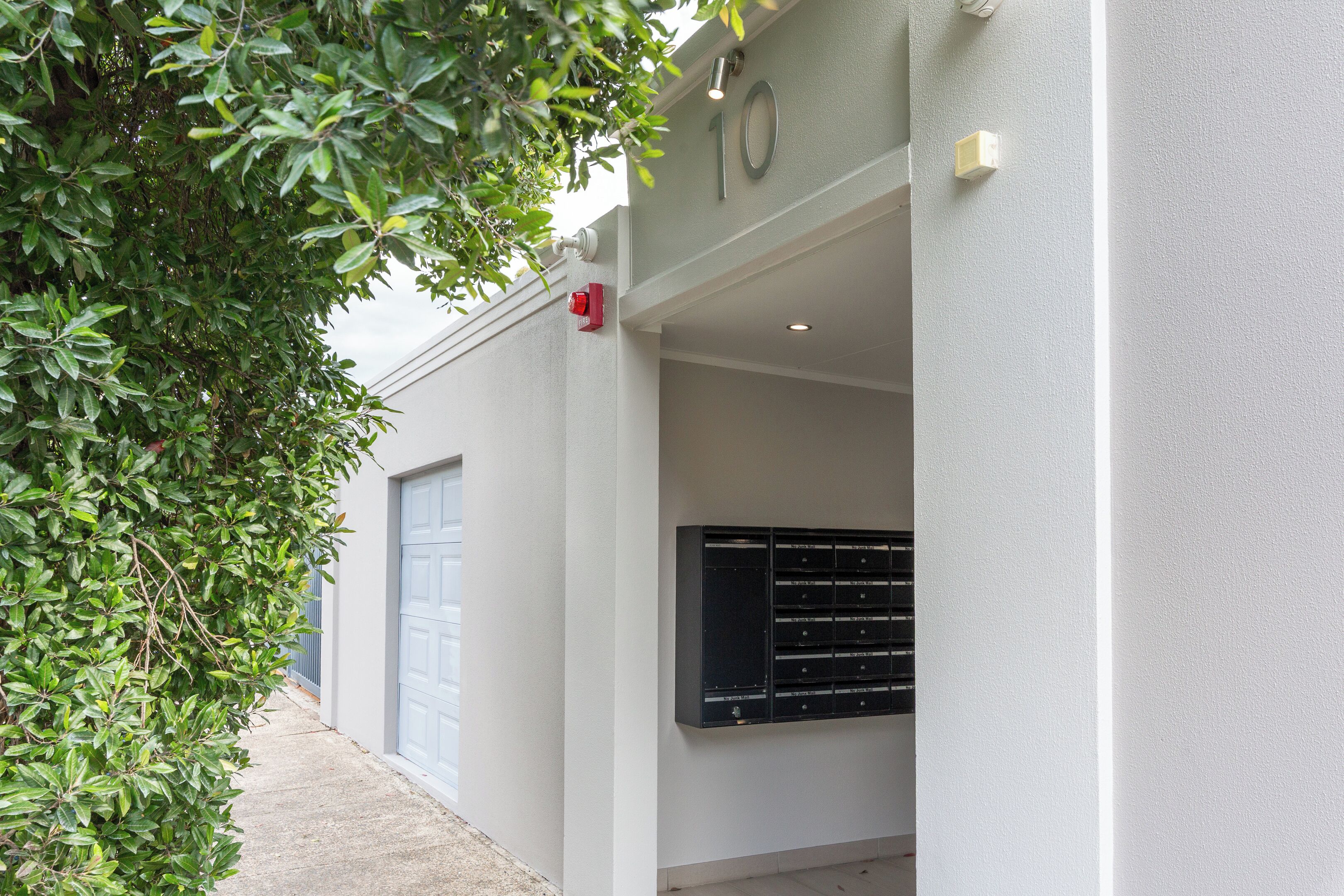 Une entrée d’immeuble avec un détecteur d’incendie, une boîte aux lettres et une porte de garage.