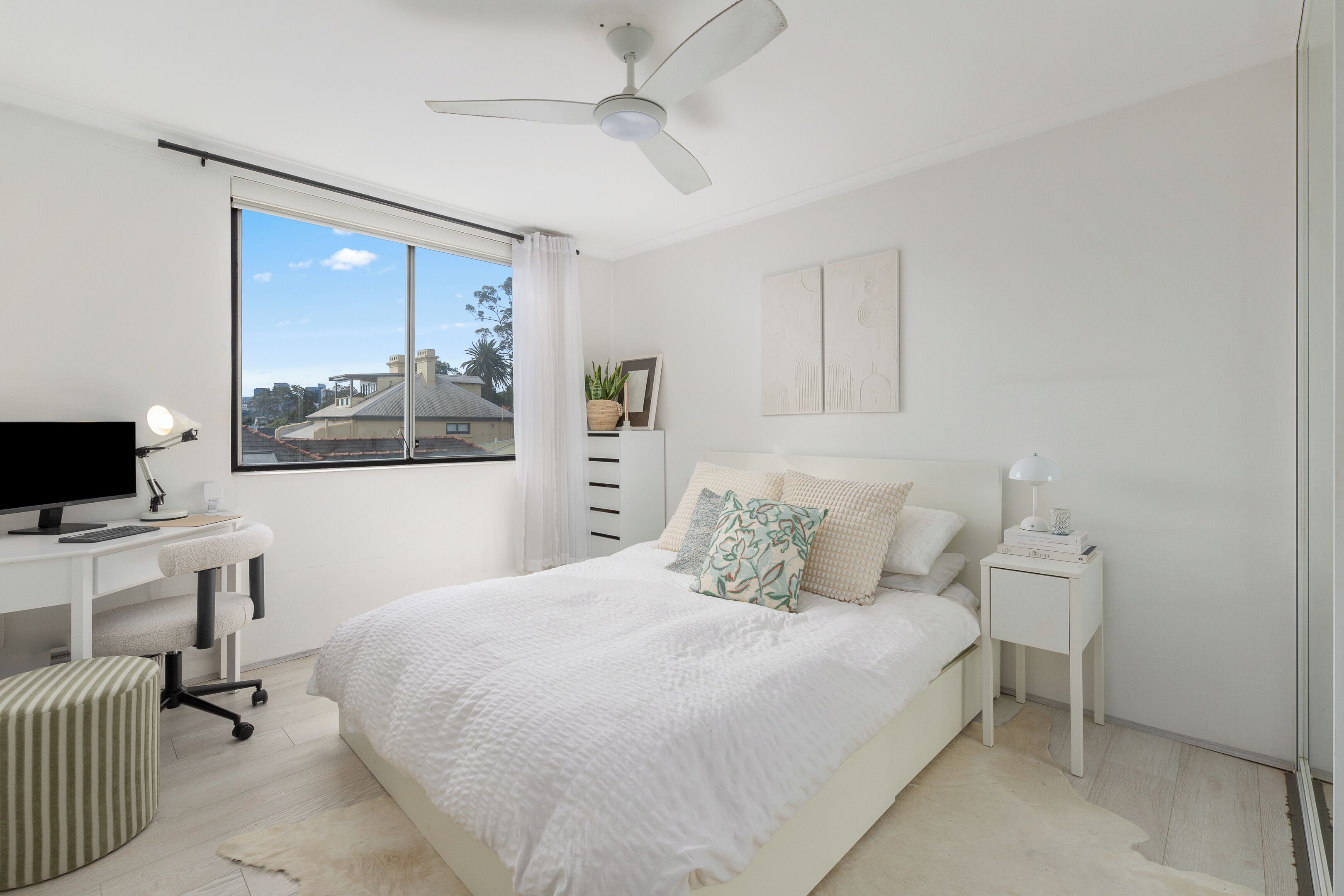 Une chambre à coucher comprenant un lit, un bureau, une chaise, une table de chevet, une lampe et un ventilateur de plafond.
