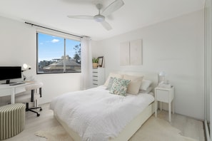 Une chambre à coucher comprenant un lit, un bureau, une chaise, une table de chevet, une lampe et un ventilateur de plafond.