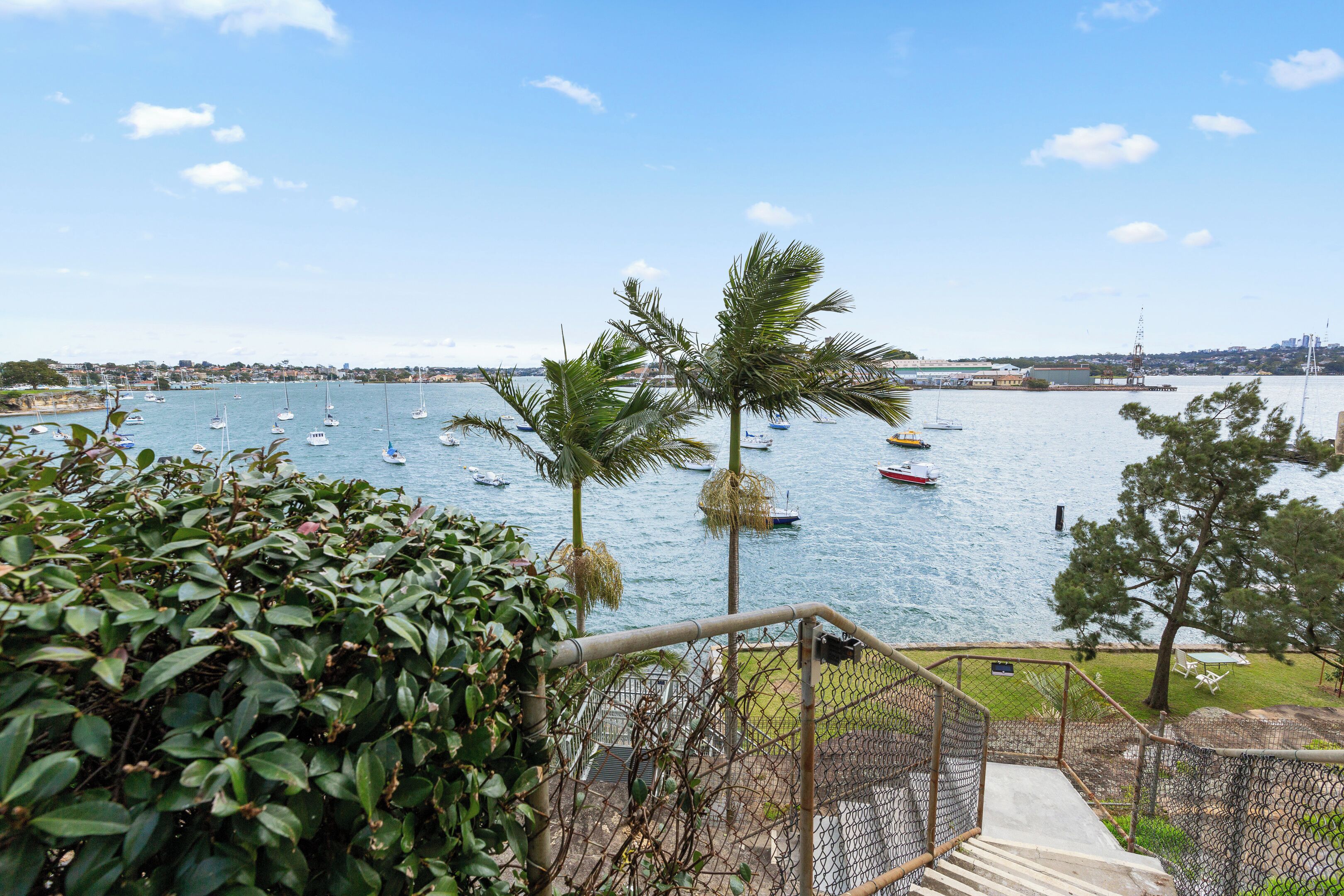 A coastal view with boats on the water, a clear sky, and a staircase leading down to the beach.