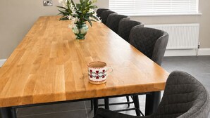 A dining area with a wooden table, grey upholstered chairs, a wall clock, and a window with blinds.