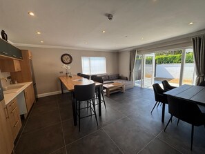 A modern kitchen with a dining area, a sofa, and a sliding glass door to the outside.