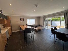 A modern kitchen with a dining area, a sofa, and a sliding glass door to the outside.