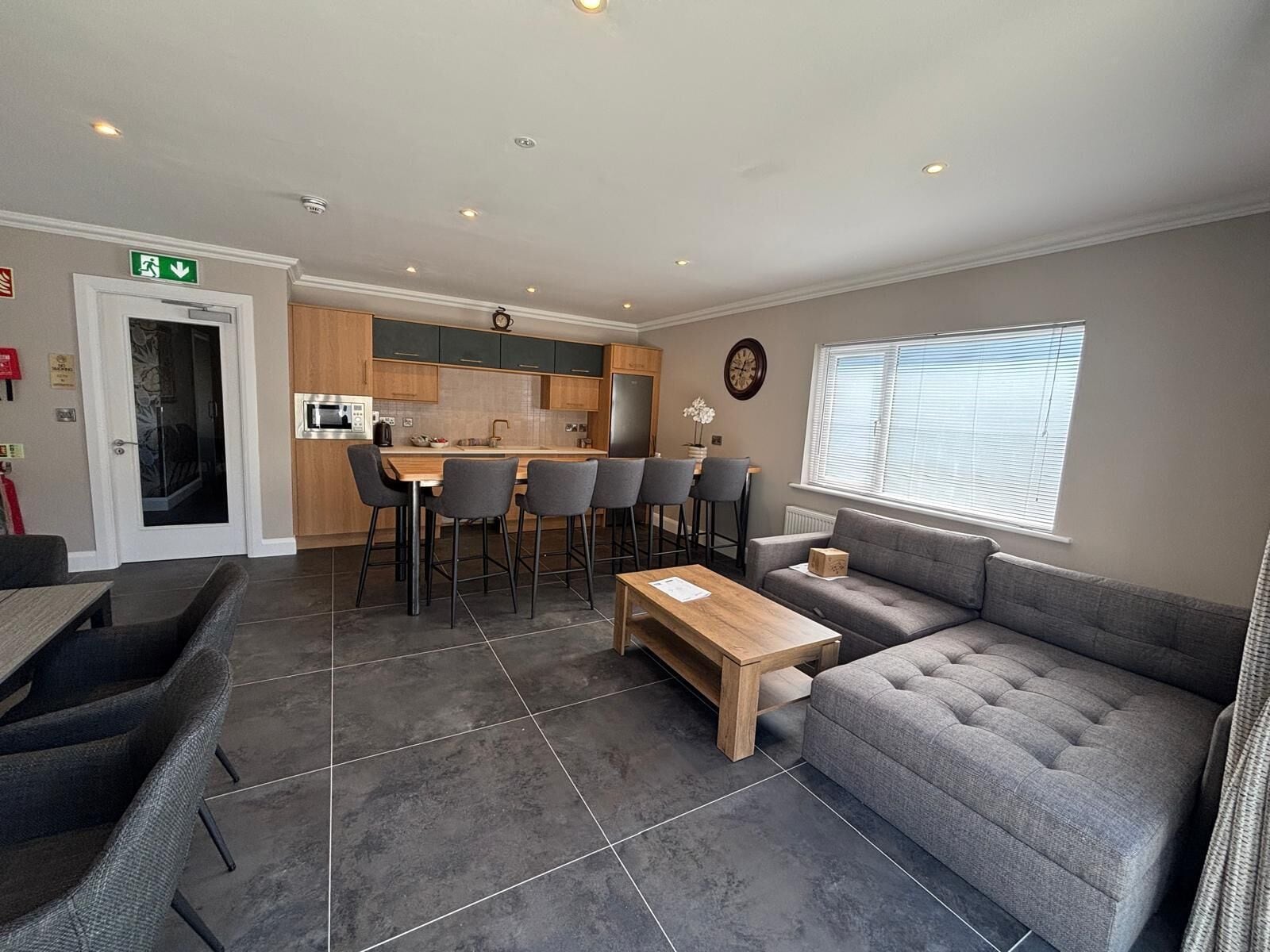 A modern living room with a grey sofa, a wooden coffee table, and a kitchen area with a dining set.