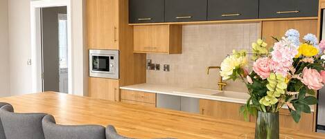 A modern kitchen with a wooden countertop, bar stools, and a vase of flowers.