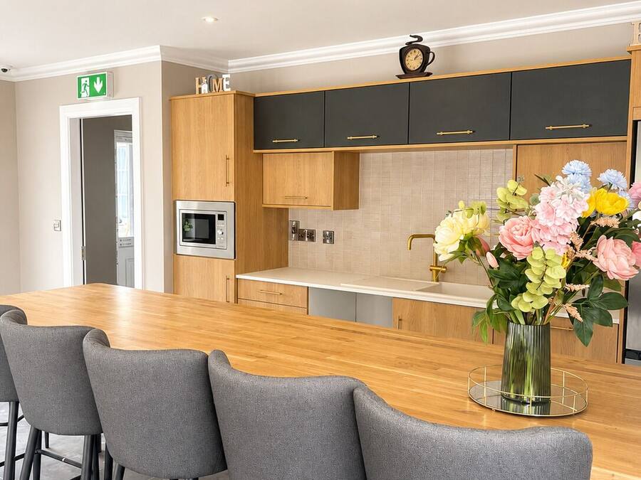 Una cocina moderna con encimera de madera, taburetes de bar y un florero con flores.
