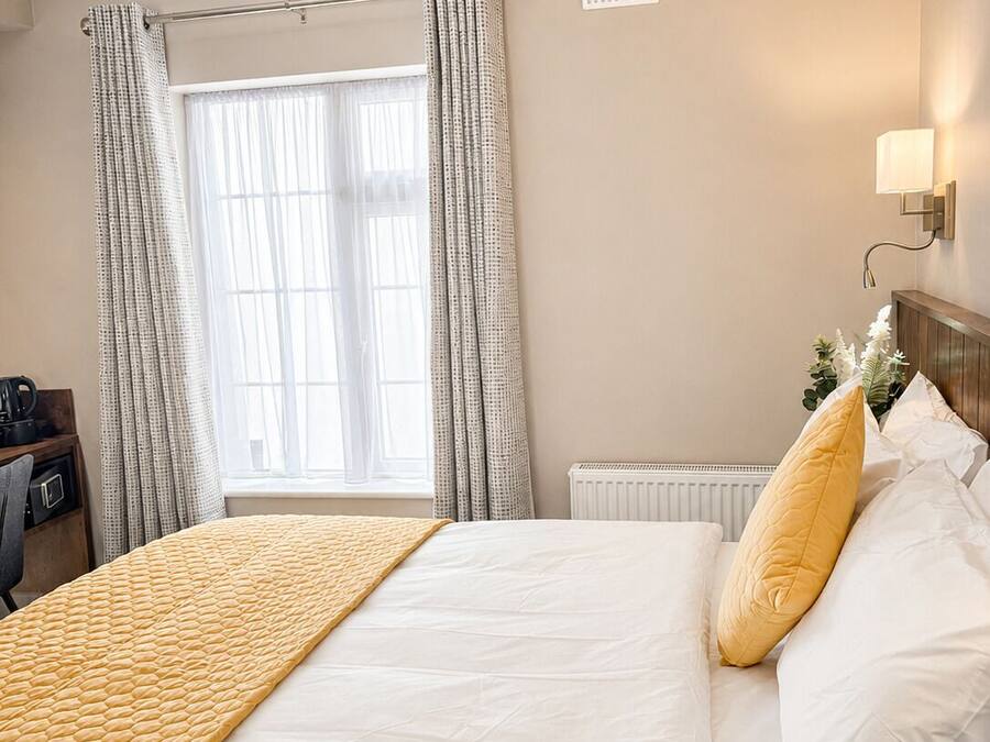 Hotellihuone, jossa on sänky, työpöytä tuolilla, patteri ja ikkuna, jossa on verhot.