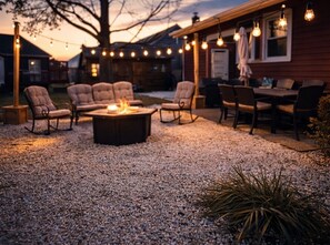 Un espace extérieur aménagé avec un foyer, des chaises et des guirlandes lumineuses.