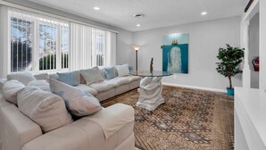 Un salon moderne avec un canapé d’angle beige, une table basse en verre et un tapis à motifs.