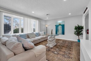 A modern living room with a beige sectional sofa, a glass coffee table, and a patterned rug. - Relaxed Ocean Gate Shore Getaway 3BR + Fireplace (Ocean Gate)