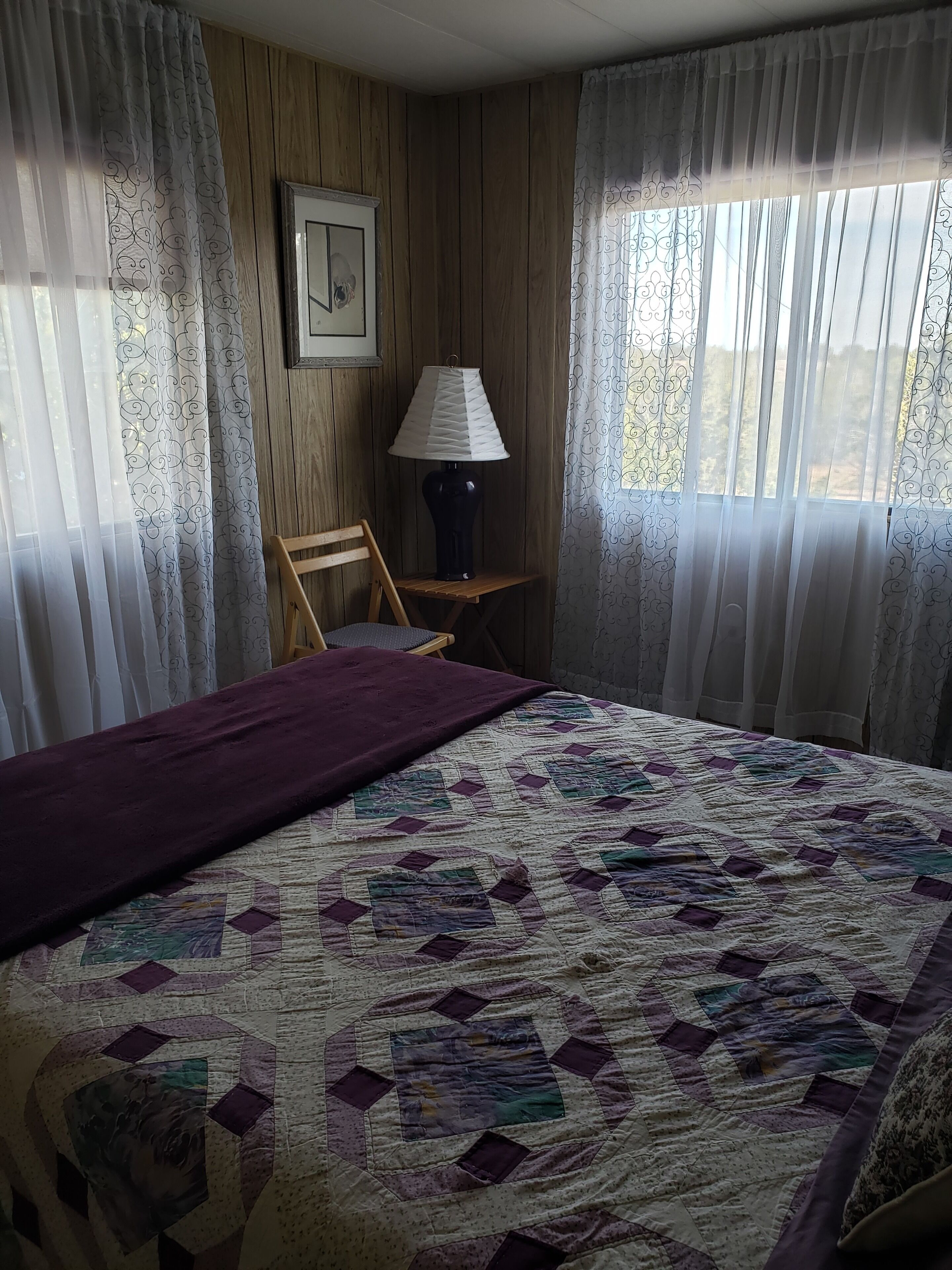 A room with a bed, a chair, a lamp, and a window with curtains.