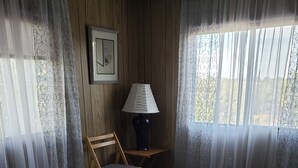 Une pièce comprenant un lit, une chaise, une lampe et une fenêtre avec des rideaux.