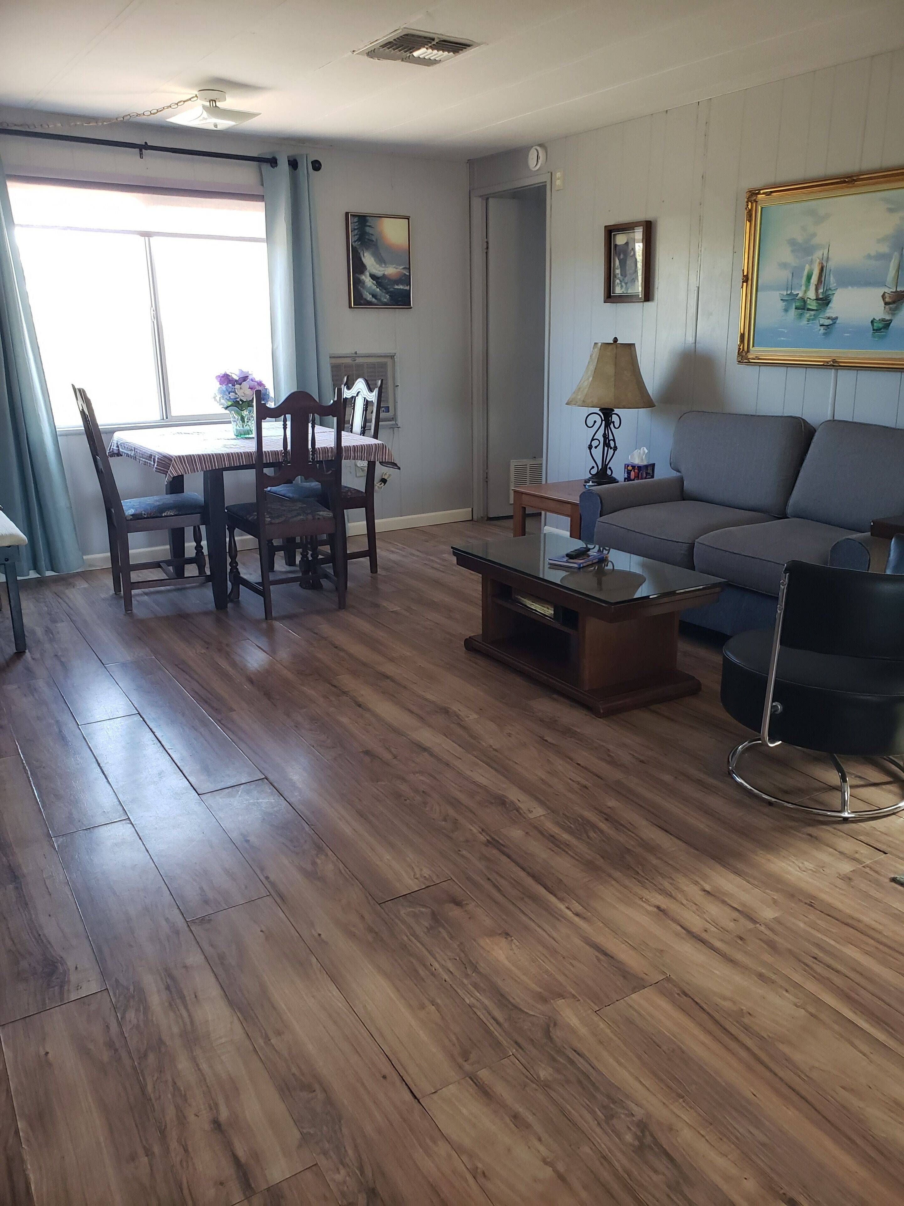A living room with a wooden floor, a sofa, a coffee table, and a dining area with chairs and a table.