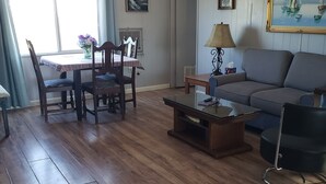 Un salon doté d’un plancher en bois, d’un canapé, d’une table basse et d’un coin repas avec des chaises et une table.