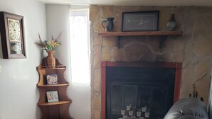 Un salon avec une cheminée, un canapé en cuir, une table d’appoint en bois sur laquelle est posé un vase, et une horloge encadrée.