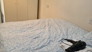 Un lit recouvert d’une couvre-lit à motifs, une paire de chaussures et une serviette pliée posées dessus.