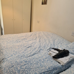 A bed with a patterned bedspread, a pair of shoes, and a folded towel on it.