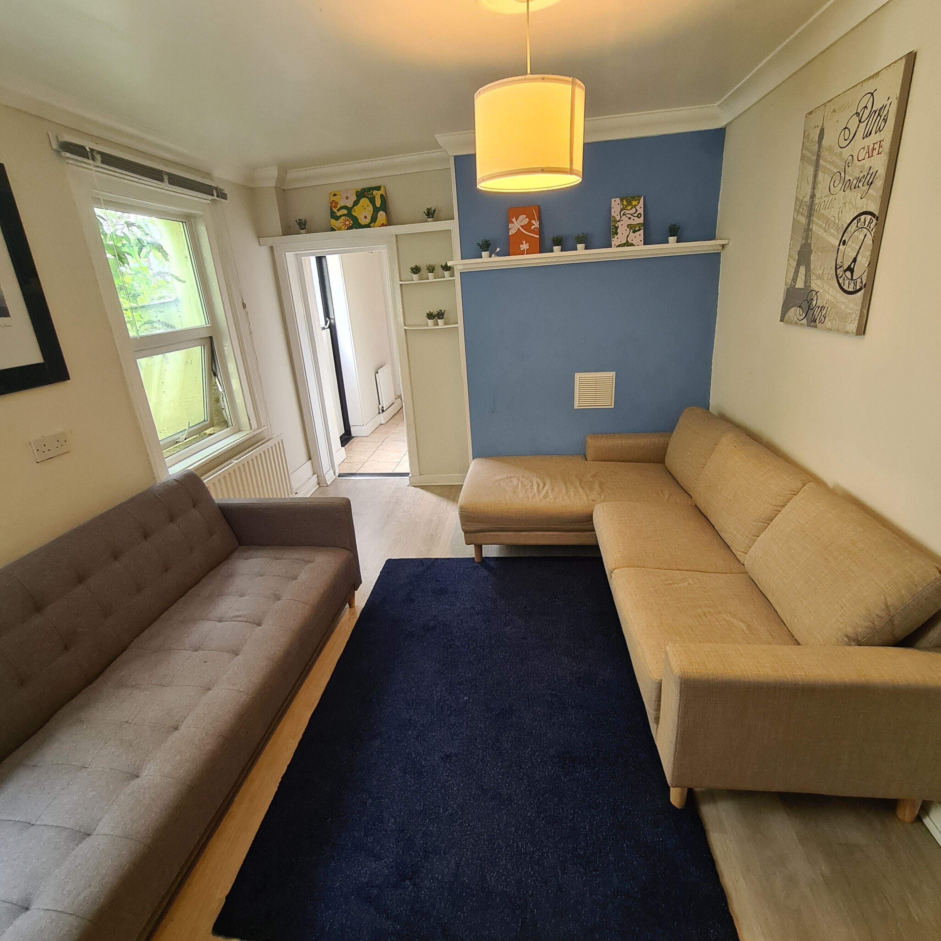A living room with a sofa, a blue rug, and a wall-mounted shelf with decorative items.