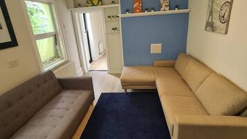A living room with a sofa, a blue rug, and a wall-mounted shelf with decorative items.
